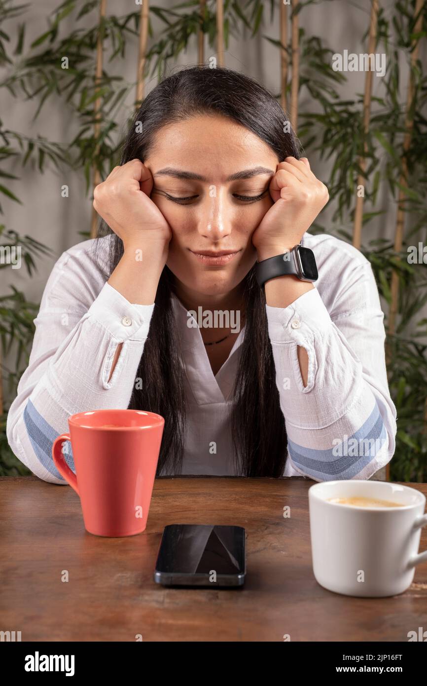 Giovane donna annoiato, ritratto di brunetta caucasica annoiato giovane donna. Seduti nel bar, bevendo una bevanda calda e guardando il suo smartphone. Foto Stock