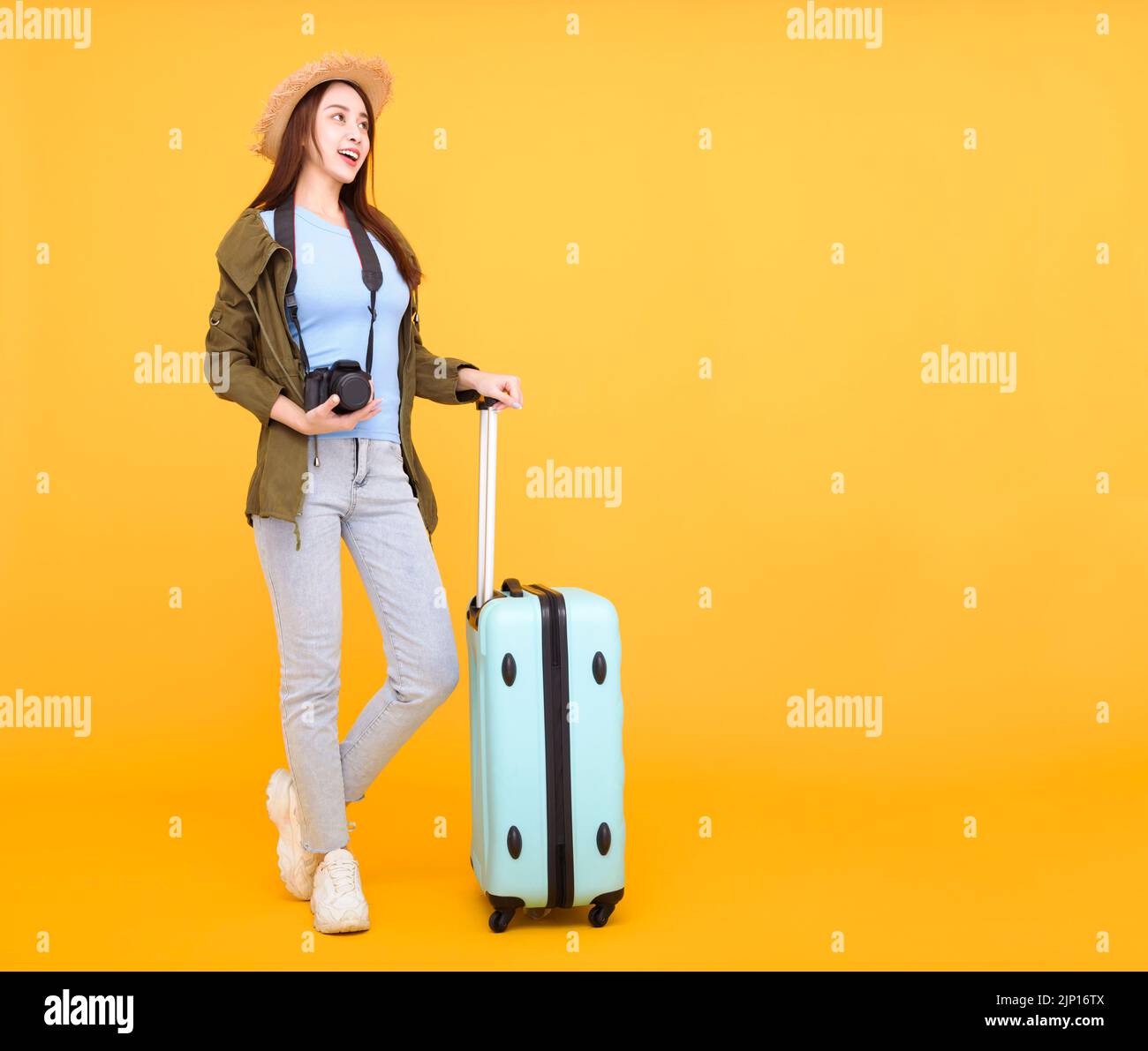 Felice giovane donna con bagagli e macchina fotografica isolato su sfondo giallo, autunno, concetto di viaggio. Foto Stock