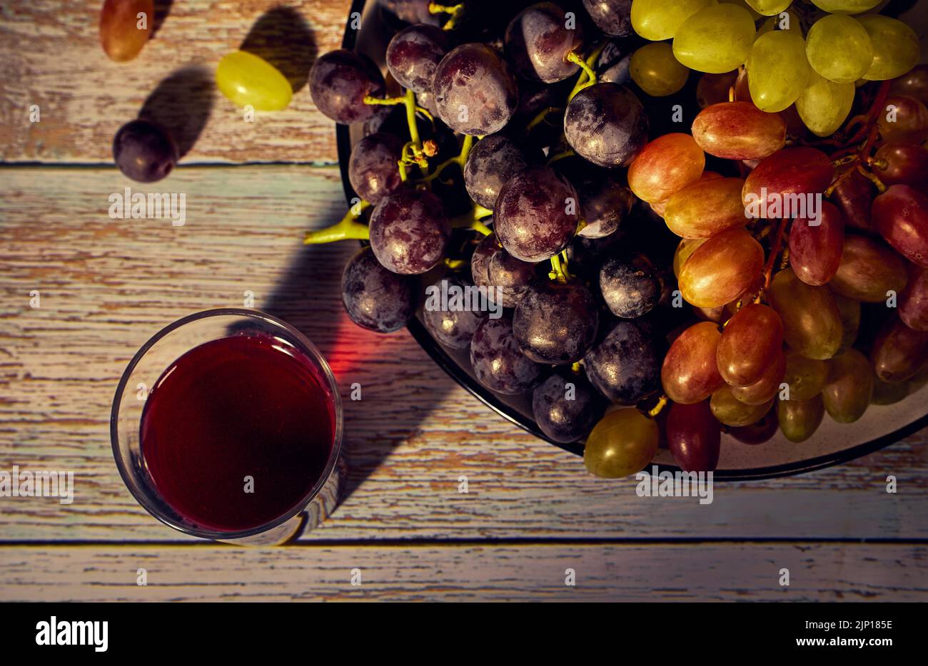 Un piatto con grappoli di uva nera, bianca e rosa e bicchiere di vino rosso Foto Stock