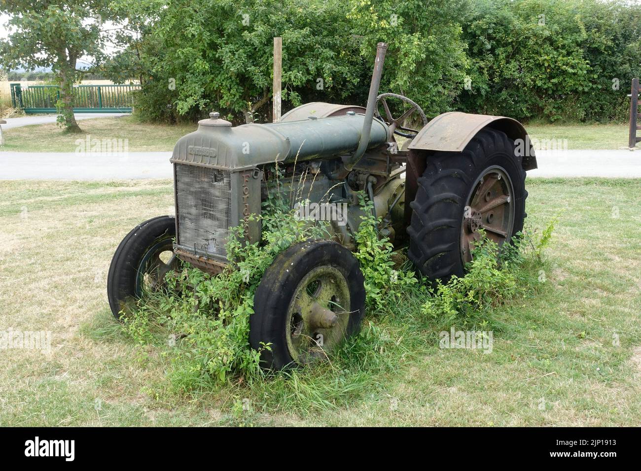 Vecchio trattore verde Fordson parcheggiato all'ingresso di fram con vegetazione che cresce su di esso Chewltenham UK Foto Stock