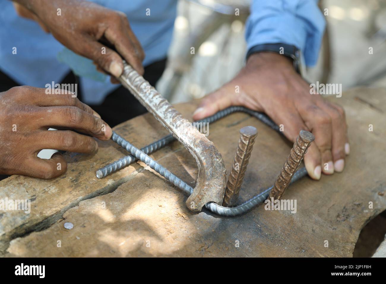 L'operatore piega l'asta di acciaio utilizzando la piegatrice in un cantiere. Colpo di primo piano di mano maschio con barra di metallo curvante con manodopera. Il lavoratore Foto Stock