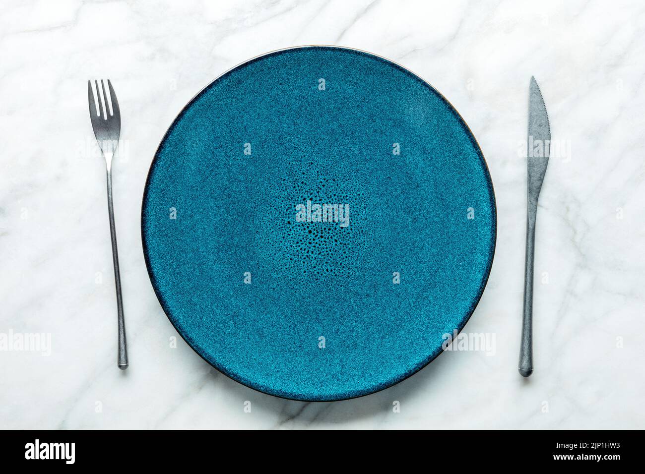 Set di stoviglie moderno con un piatto blu vivace, una forchetta e un coltello, piatto a vista. Stoviglie alla moda Foto Stock