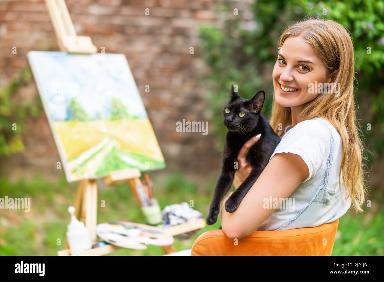 La donna ama passare il tempo con il suo gatto e dipingere su tela all'aperto. Foto Stock