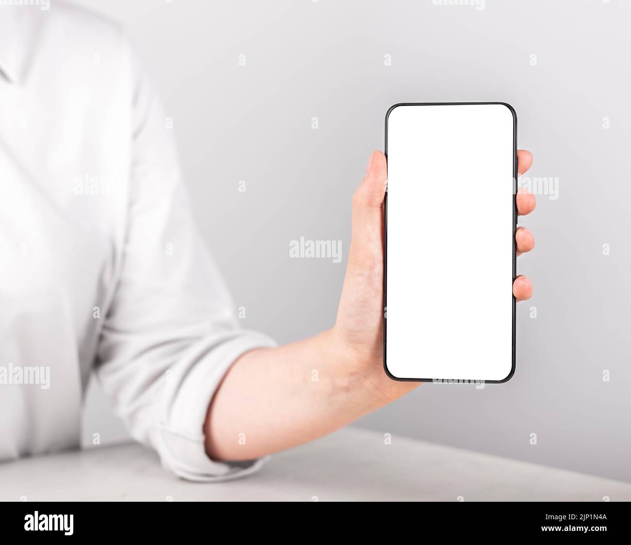 Donna che tiene il mockup del telefono in posizione verticale. Modello telefonico con schermo vuoto per la pubblicità. Donna seduta al tavolo e che mostra smth allo smartphone. Foto di alta qualità Foto Stock