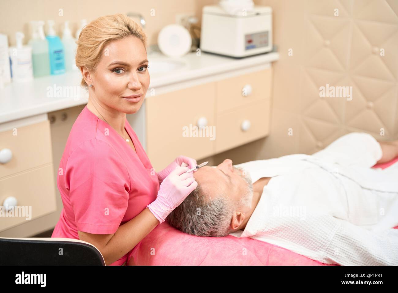 Estetista guardando la macchina fotografica e tenendo la siringa vicino alla testa dell'uomo Foto Stock