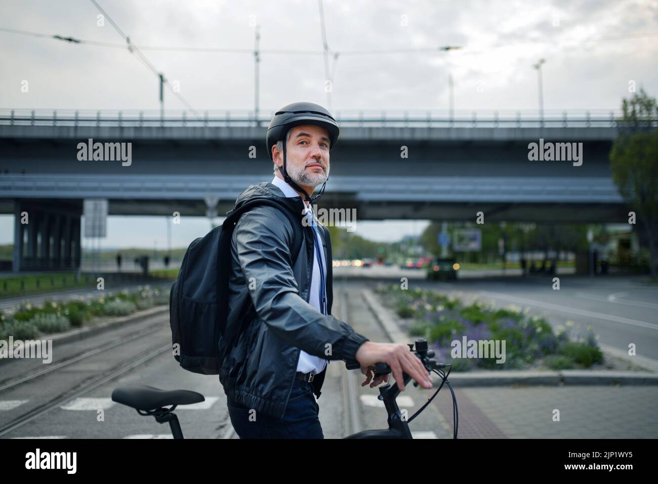 Uomo d'affari che viaggia per lavoro, attraversando la strada con la bicicletta, concetto di stile di vita sostenibile. Foto Stock