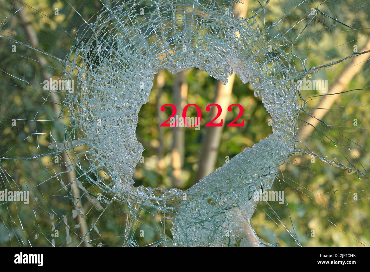 Duro e tragico 2022 anno. Guerra. Un foro nel vetro o nella finestra. Finestra rotta che si affaccia sulla foresta verde. Un buco da un guscio o proiettile nel vetro Foto Stock
