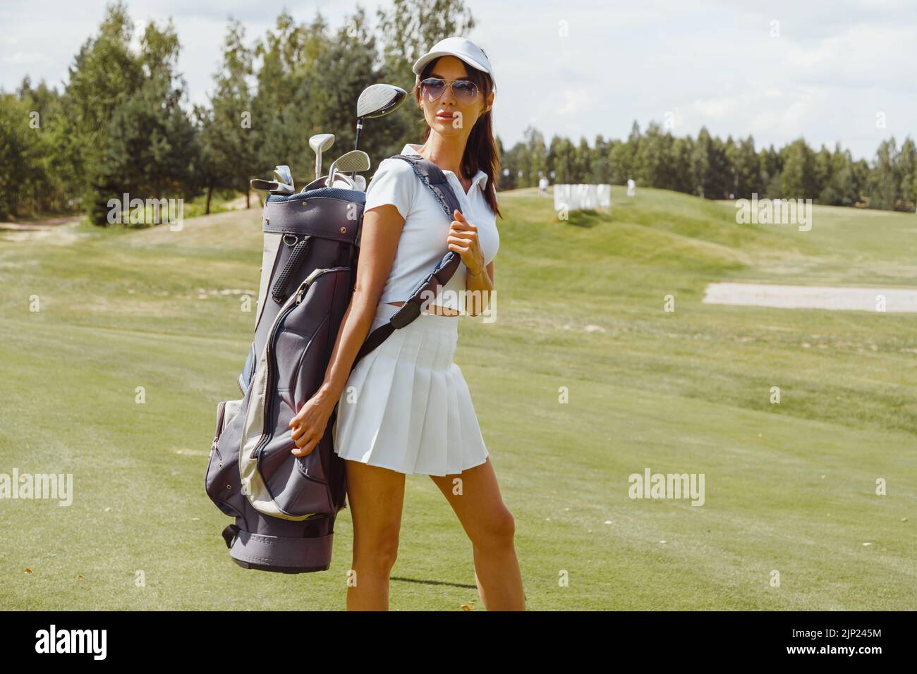Giovane donna golfer in bianco che trasporta una borsa da golf e che guarda verso Foto Stock