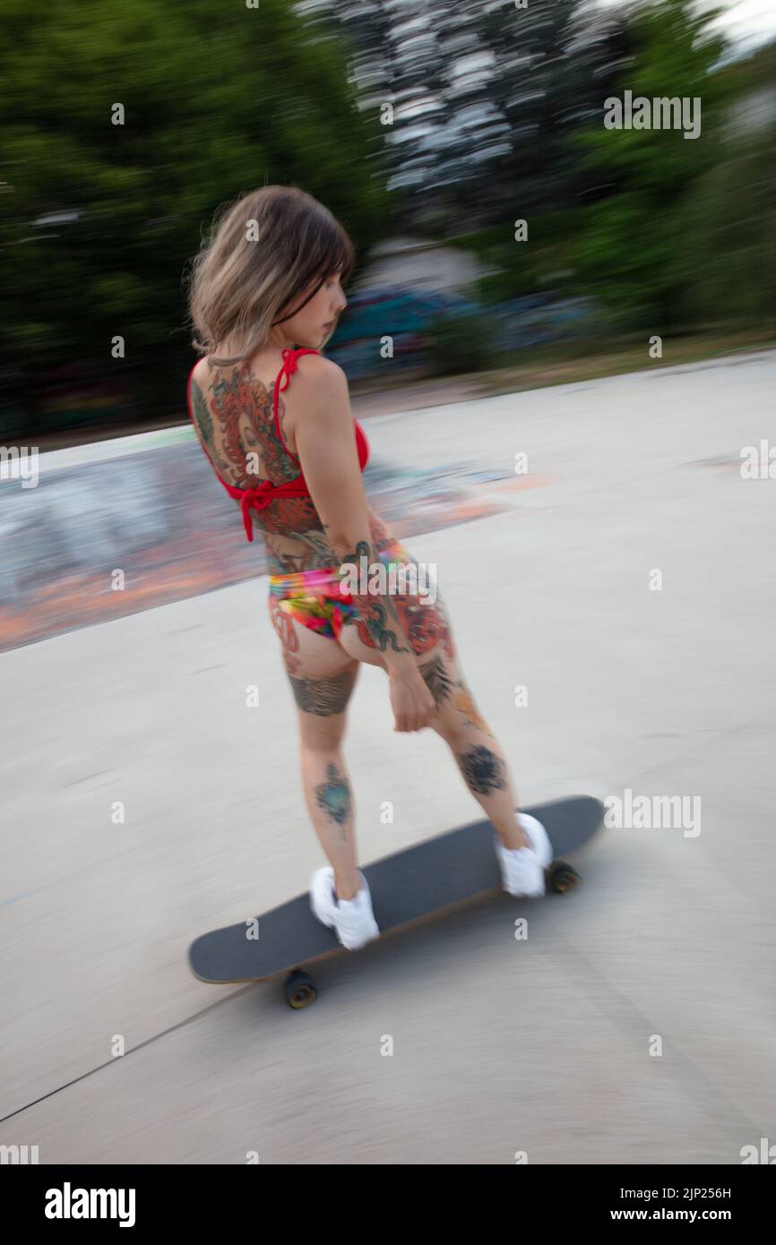 un bellissimo modello tatuato con skateboard/longboard, in bikini, skateboard allo skatepark Foto Stock
