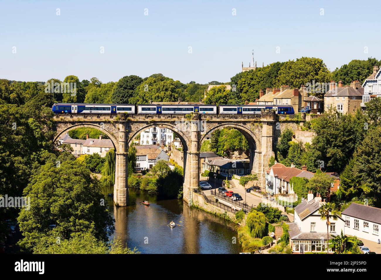 Treni del Nord che attraversano il viadotto ferroviario sul fiume Nidd, Knaresborough, North Yorkshire, Inghilterra. Calda giornata estiva con persone in barca nella r Foto Stock