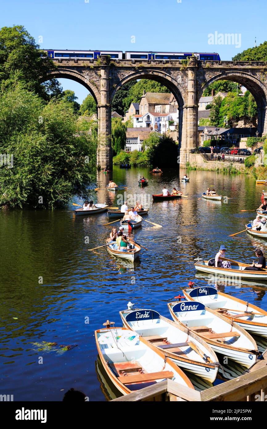 Treni del Nord che attraversano il viadotto ferroviario sul fiume Nidd, Knaresborough, North Yorkshire, Inghilterra. Calda giornata estiva con persone in barca nella r Foto Stock