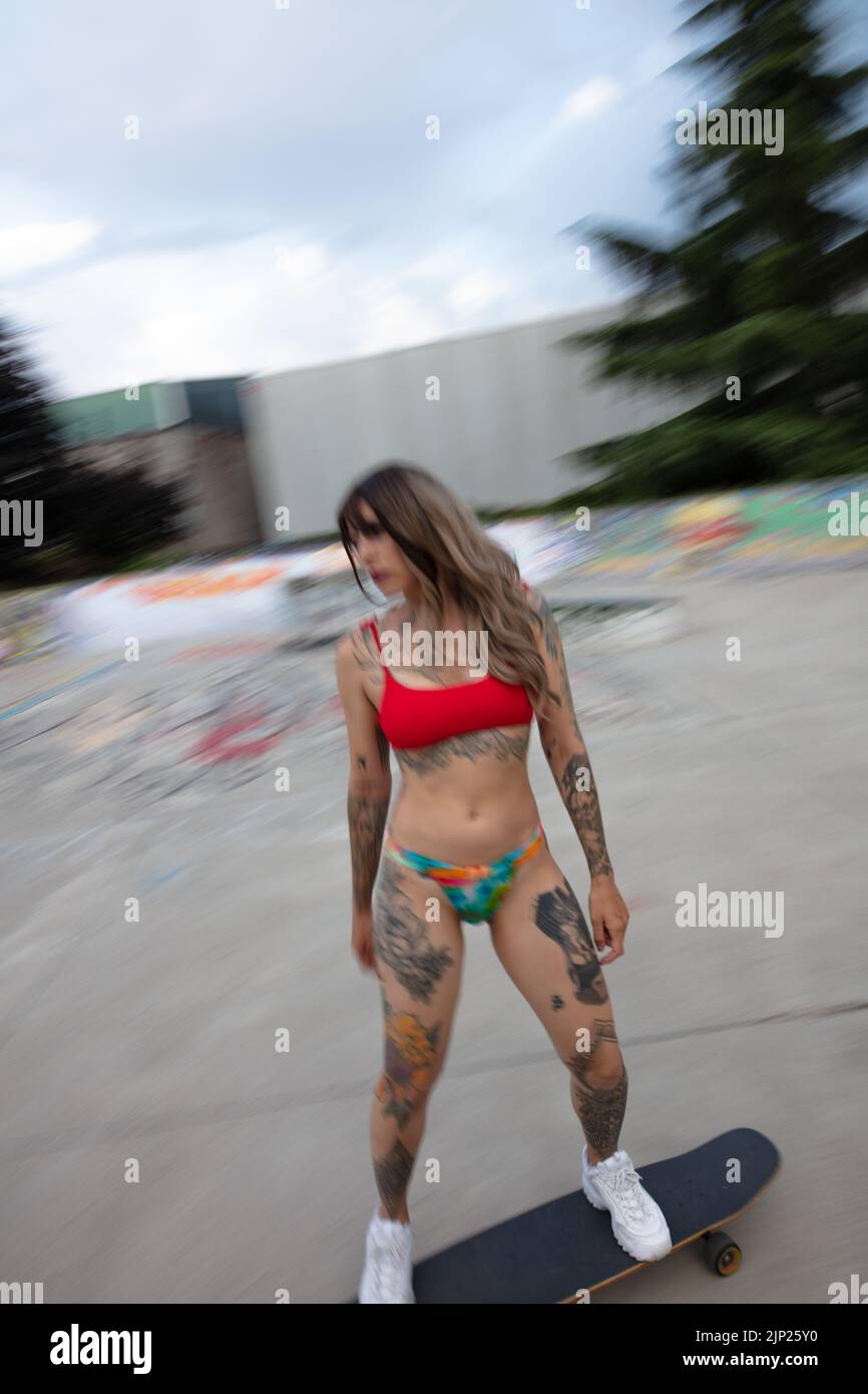 un bellissimo modello tatuato con skateboard/longboard, in bikini, skateboard allo skatepark Foto Stock