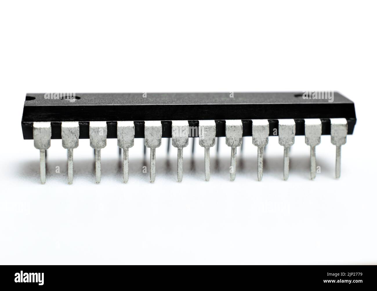 Microchip nero con piedini in metallo su sfondo bianco. Microcircuito, chip di silicio. Foto macro. Parte della scheda madre di un computer. Foto Stock
