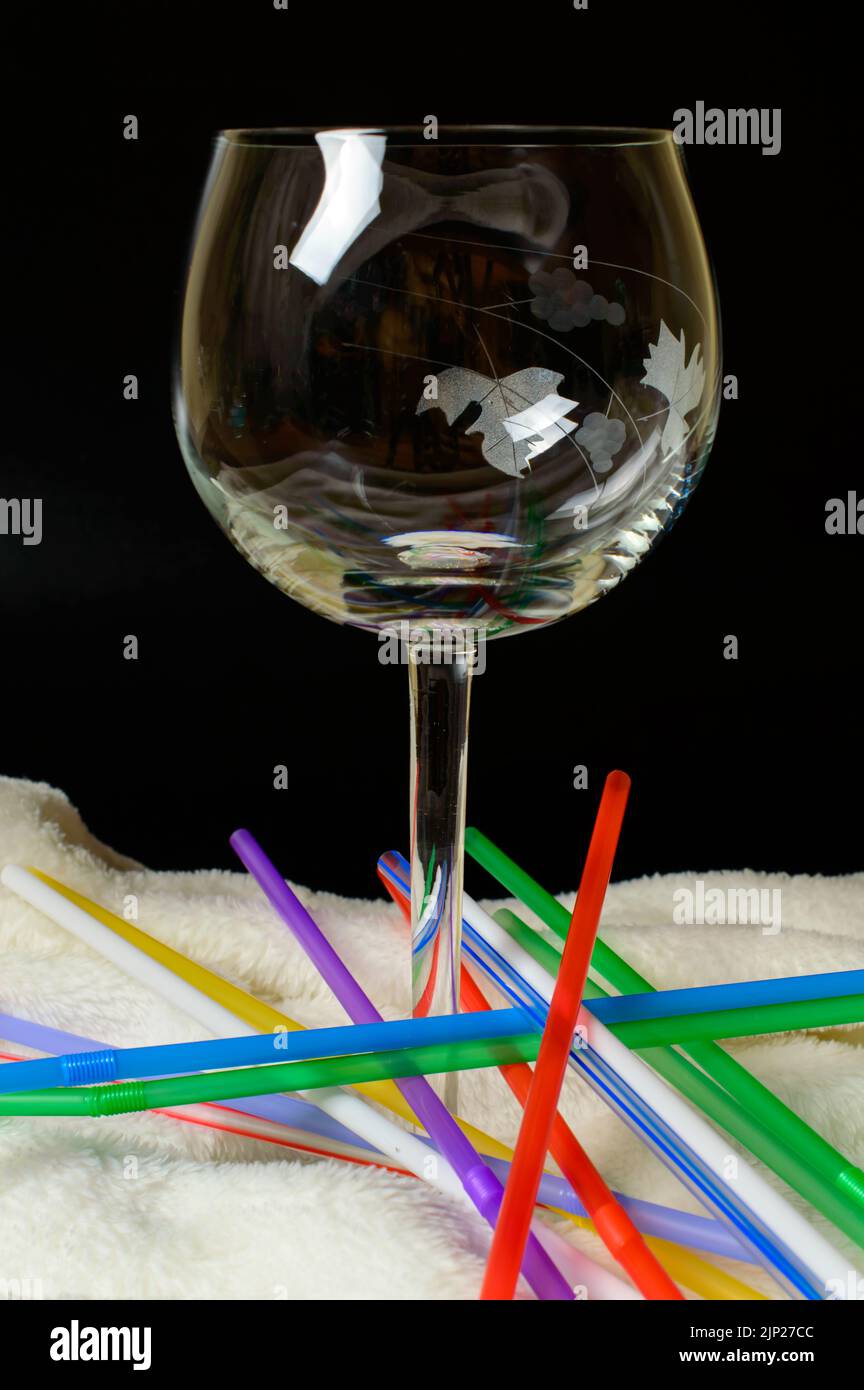 Bicchiere di vino vuoto su una morbida coperta con cannucce colorate. Composizione astratta. Concetto di cocktail alcolico. Foto Stock