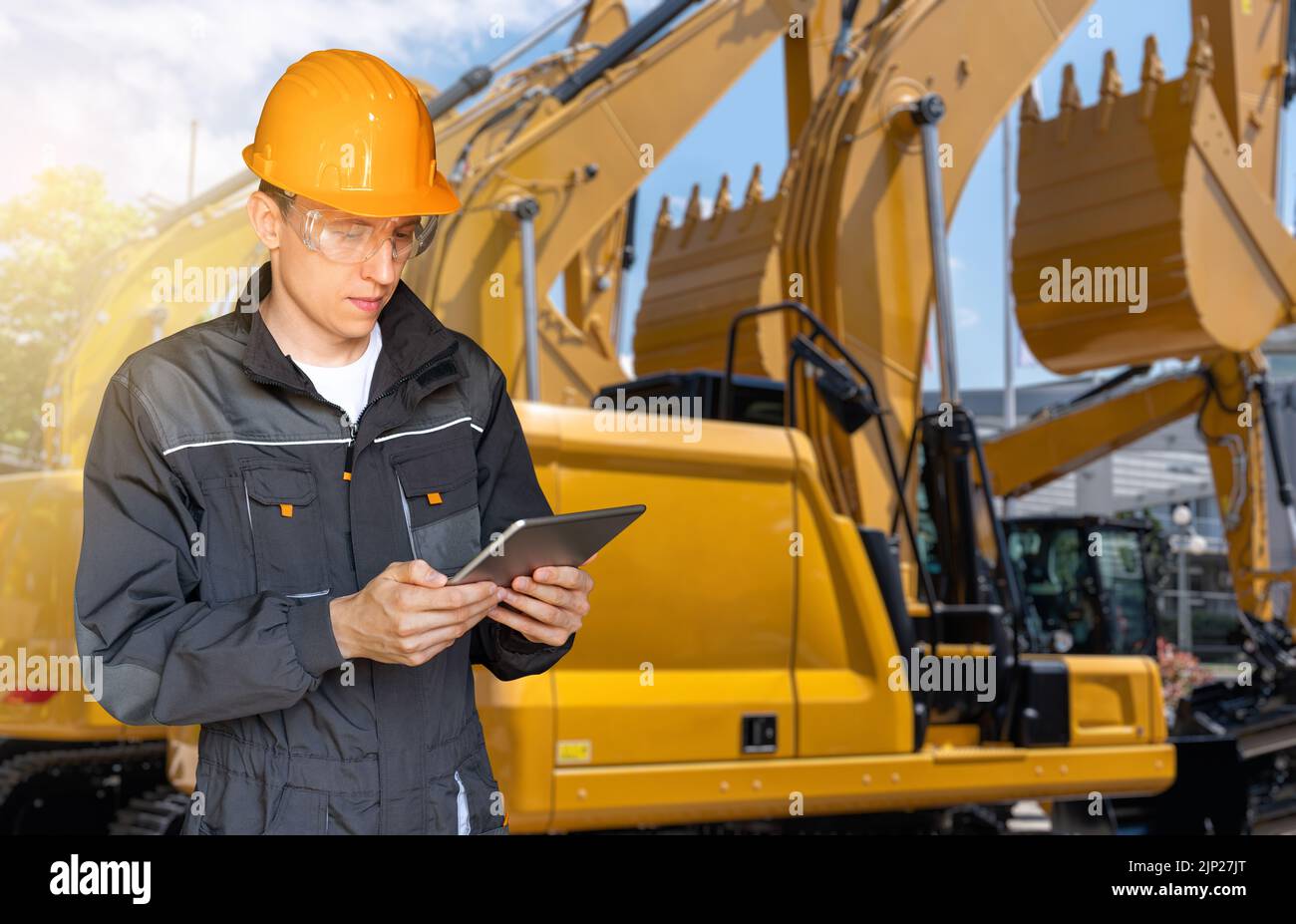 Ingegnere in un casco con un tablet digitale sullo sfondo di macchine da cantiere Foto Stock