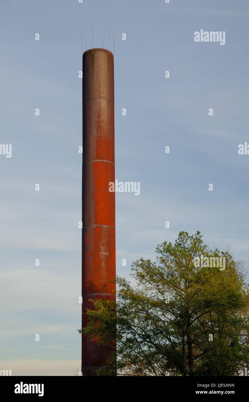 Uno stack industriale di fumo e albero contro il cielo diurno. Foto Stock