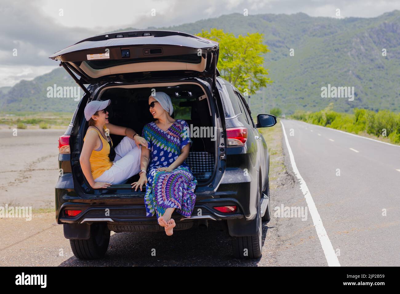 Due donne che si siedono al bagagliaio dell'auto in viaggio. Foto Stock