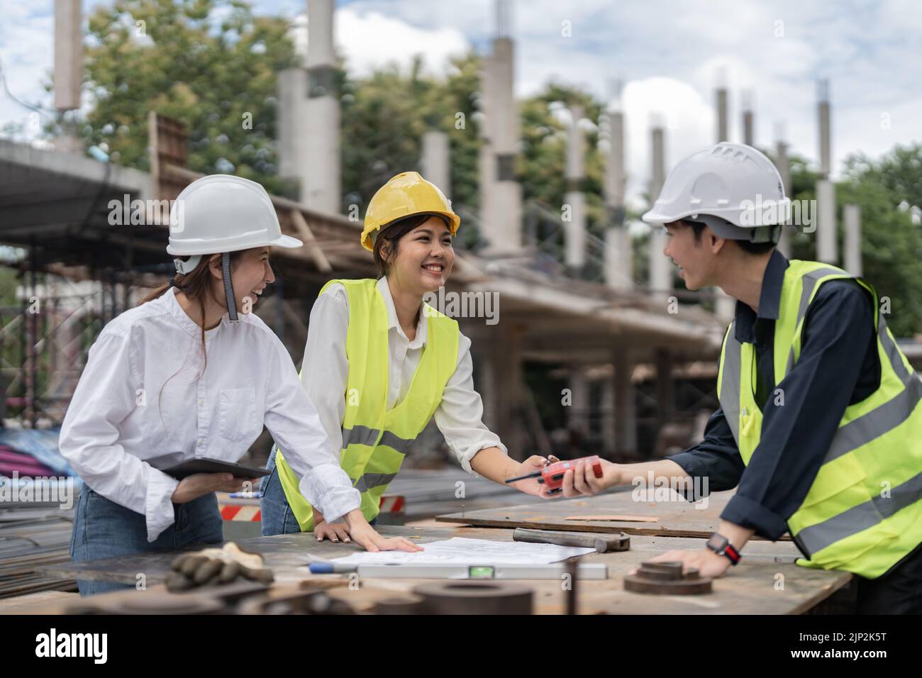 Tre colleghi che discutono del lavoro dei dati e del tablet, del notebook e del progetto di architettura in cantiere Foto Stock
