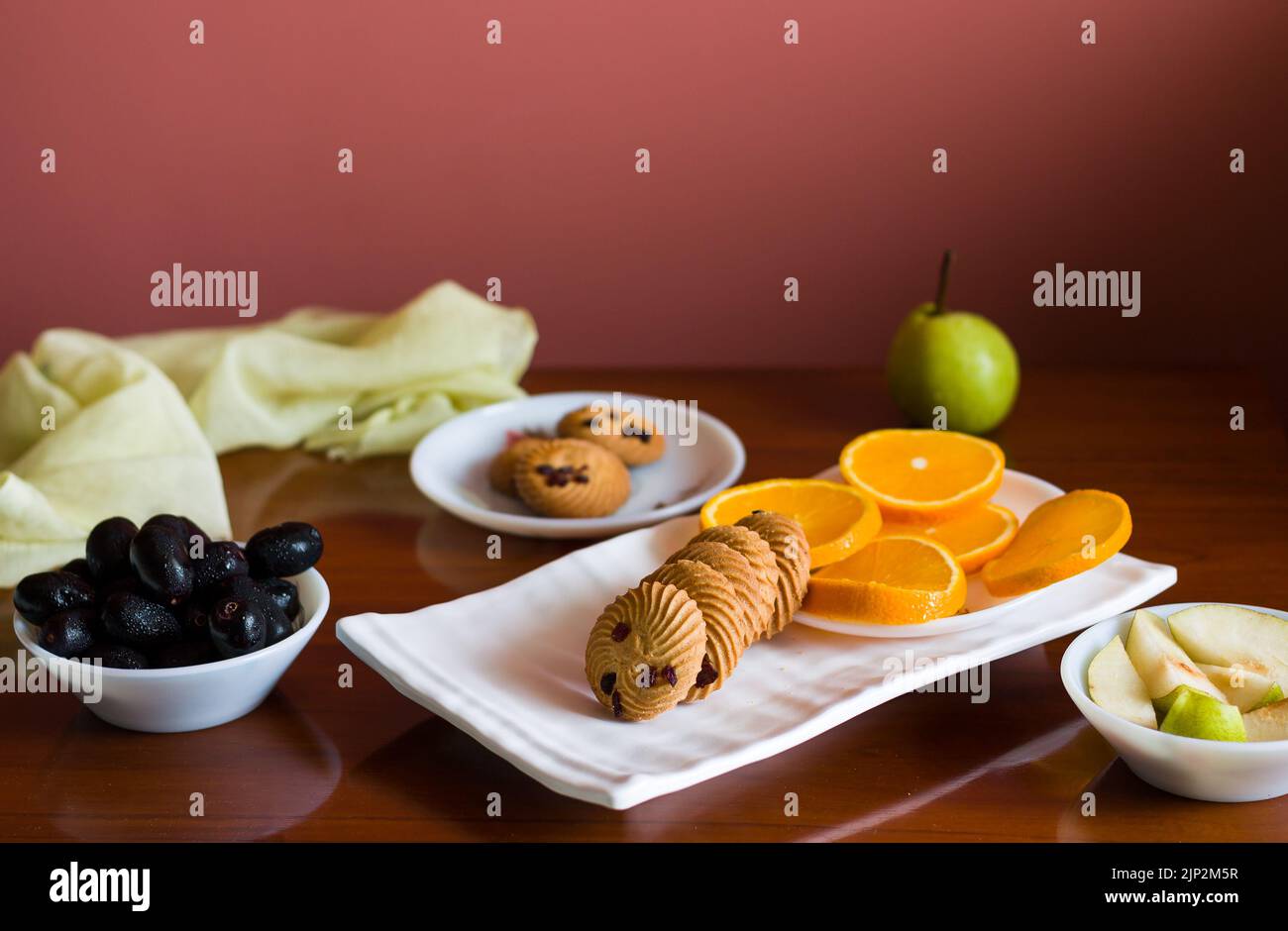 Vassoio di frutta con un mix di arance fresche, succose, dolci, pere, jamun chiamato anche bacche di prugna java e biscotti d'avena posti su un tavolo di legno scuro come b Foto Stock