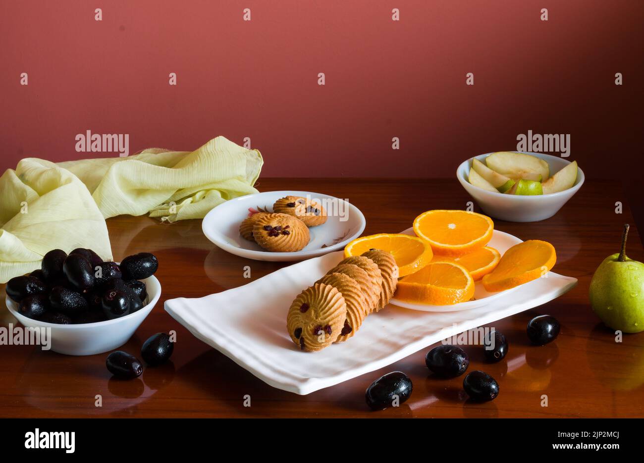 Vassoio di frutta con un mix di arance fresche, succose, dolci, pere, jamun chiamato anche bacche di prugna java e biscotti d'avena posti su un tavolo di legno scuro come b Foto Stock