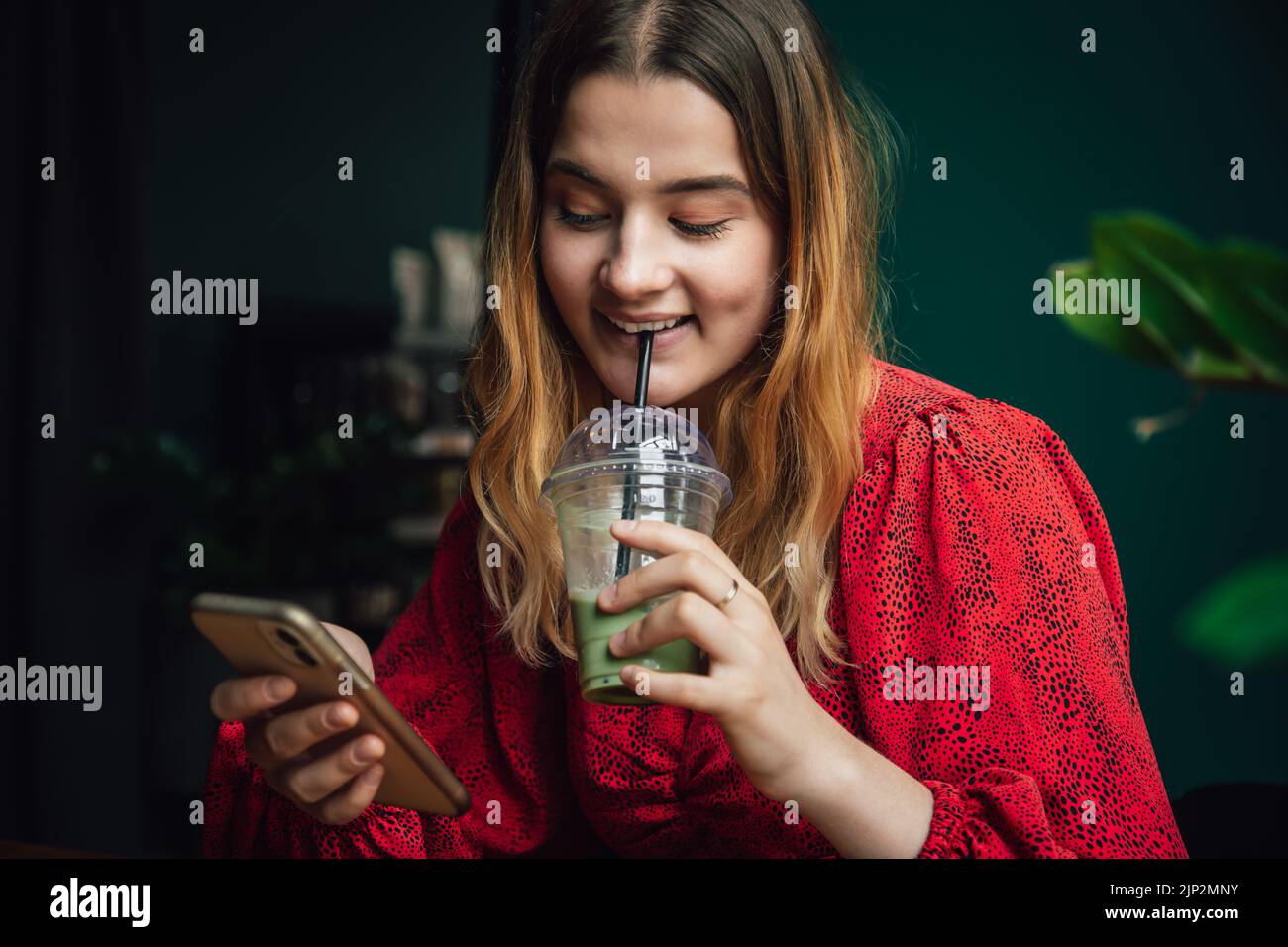 Giovane donna che beve verde bere ghiaccio matcha latte in caffè e utilizzando smartphone. Foto Stock