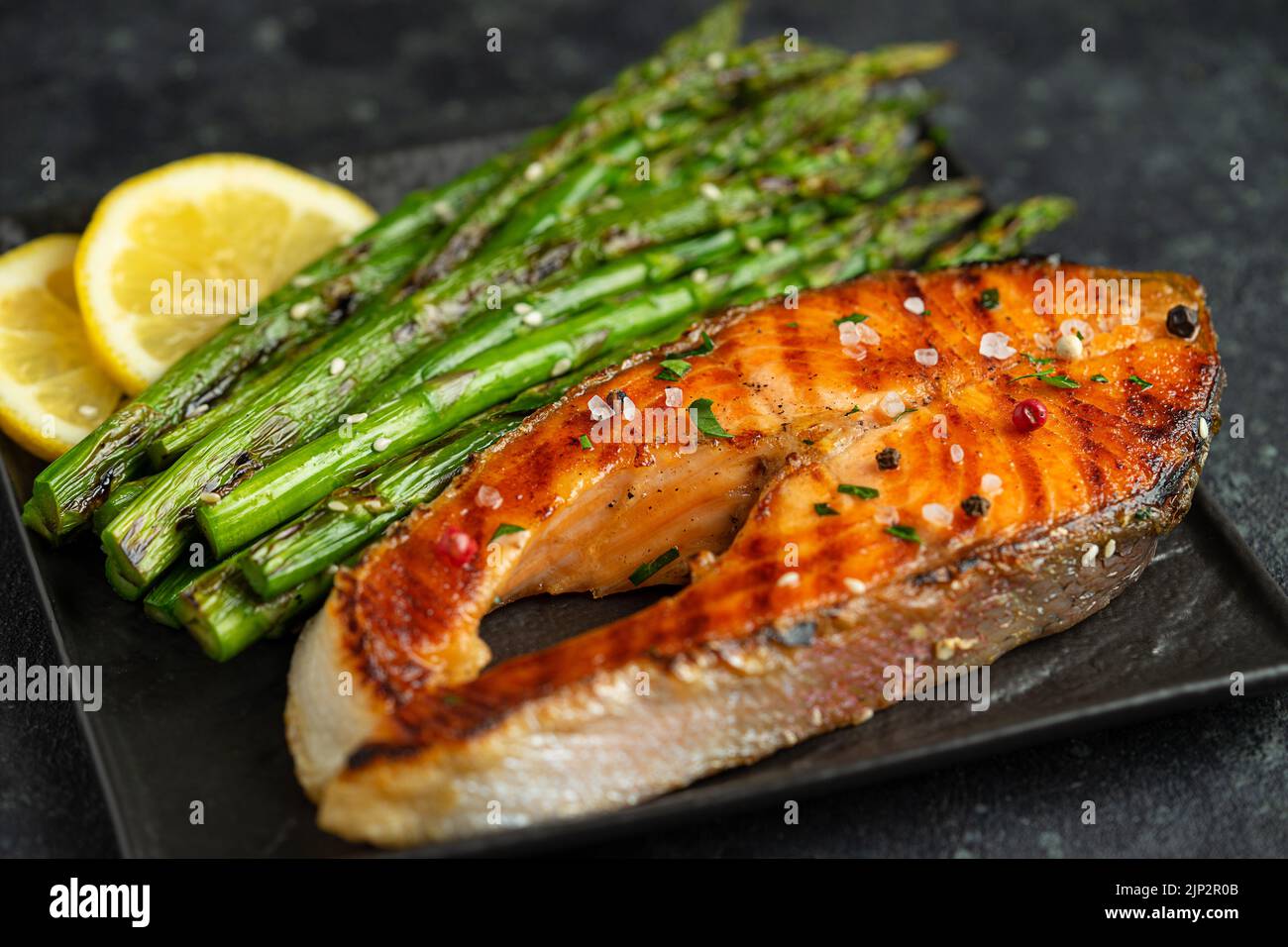 Bistecca di salmone alla griglia e asparagi sulla griglia su fondo scuro. Primo piano Foto Stock