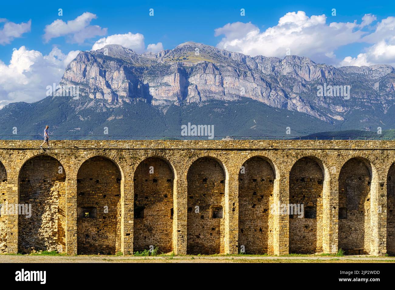 Medievale archi in pietra acquedotto fortezza con la montagna dei Pirenei sullo sfondo e le nuvole sopra il cielo blu. Ainsa, Spagna, Foto Stock