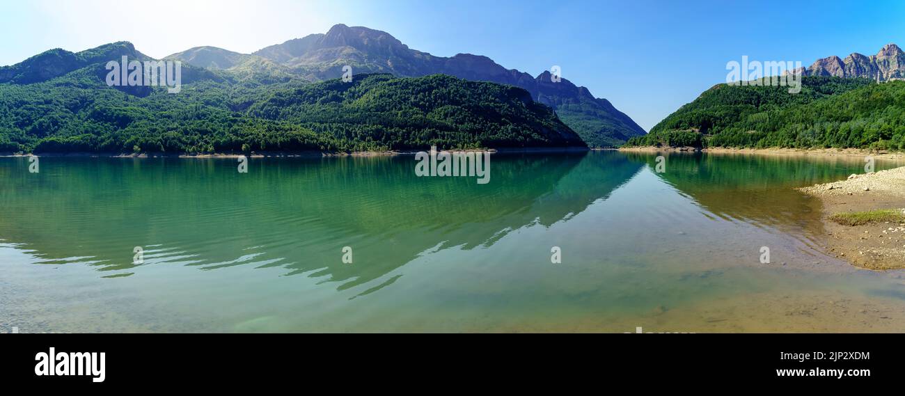 Verde paesaggio con lago e alte montagne che si riflettono nell'acqua, cielo blu e sole flare. Vista panoramica. Pirenei, Aragona, Spagna. Europa. Foto Stock