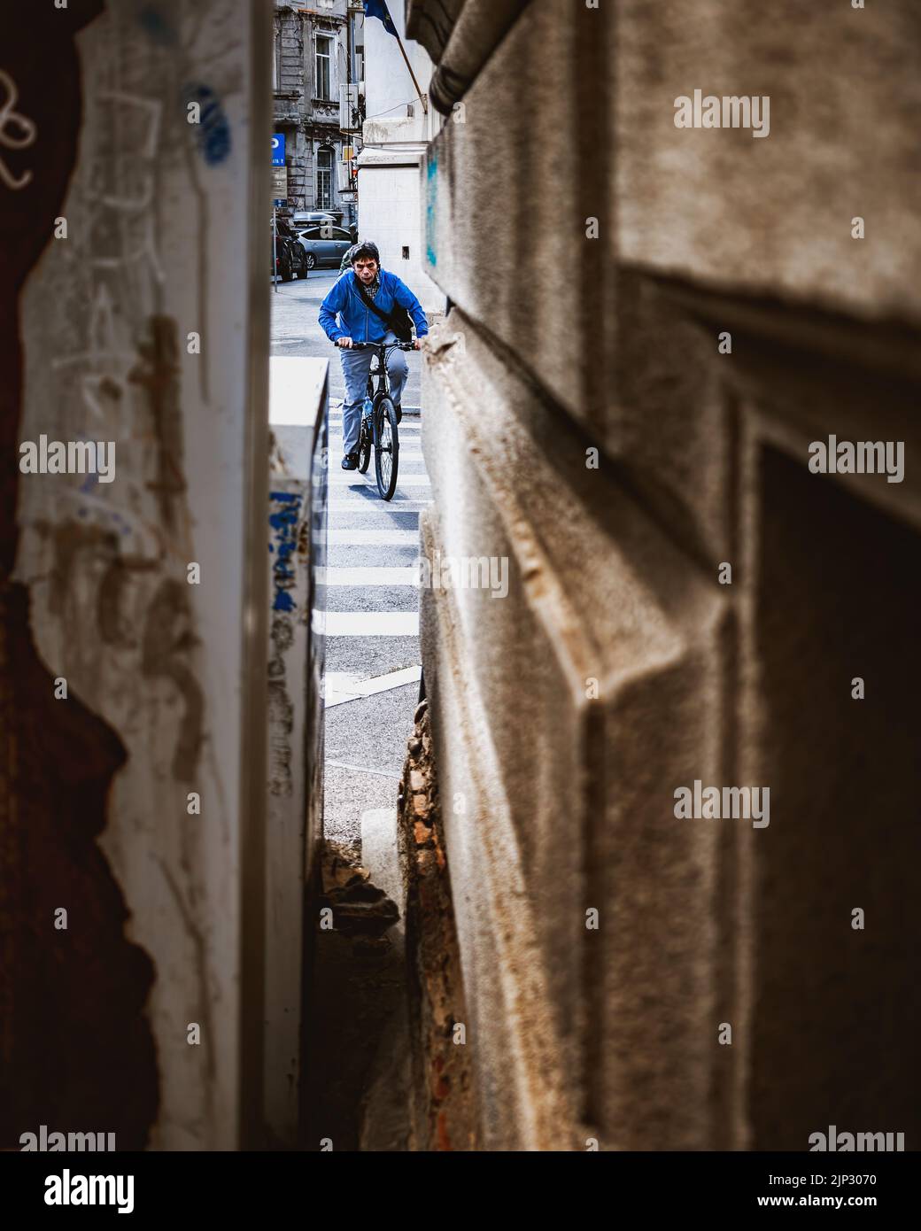 Un uomo in una camicia blu visibile dal piccolo buco tra gli edifici in bicicletta per le strade di Bucarest Foto Stock