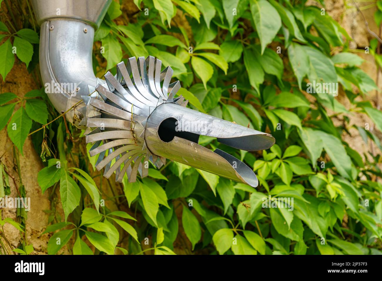 Scarico in acciaio con una forma strana che sembra un drago su uno sfondo verde edera. Foto Stock