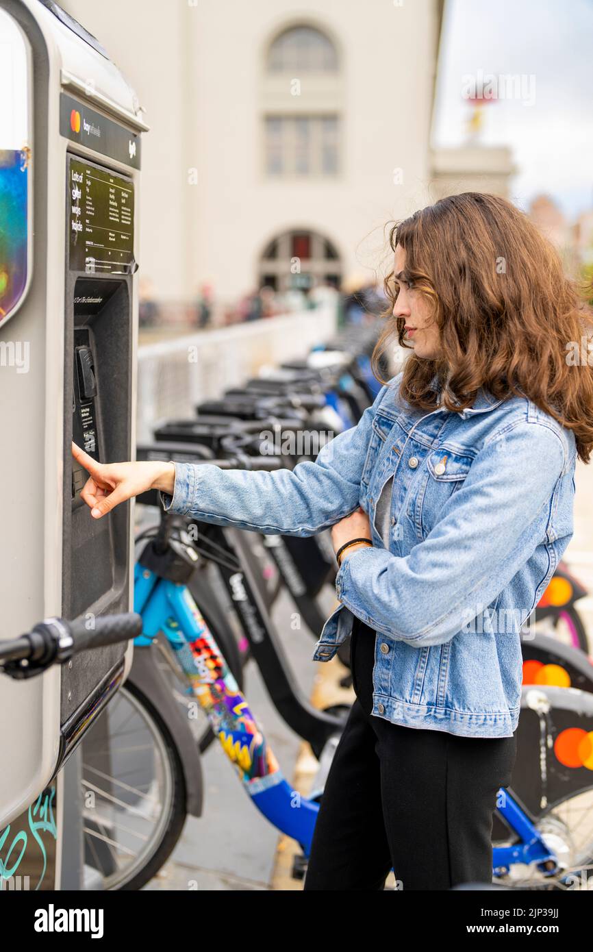 Giovane donna affittare una bicicletta elettrica | Noleggio biciclette | Trasporti | Noleggio bici | Ritratti senza posa Foto Stock