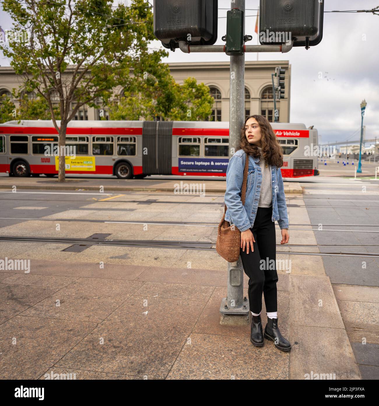Ritratto senza posa di una bella giovane donna in attesa di attraversare una strada occupato Downtown | giacca in denim | San Francisco Wharf Foto Stock