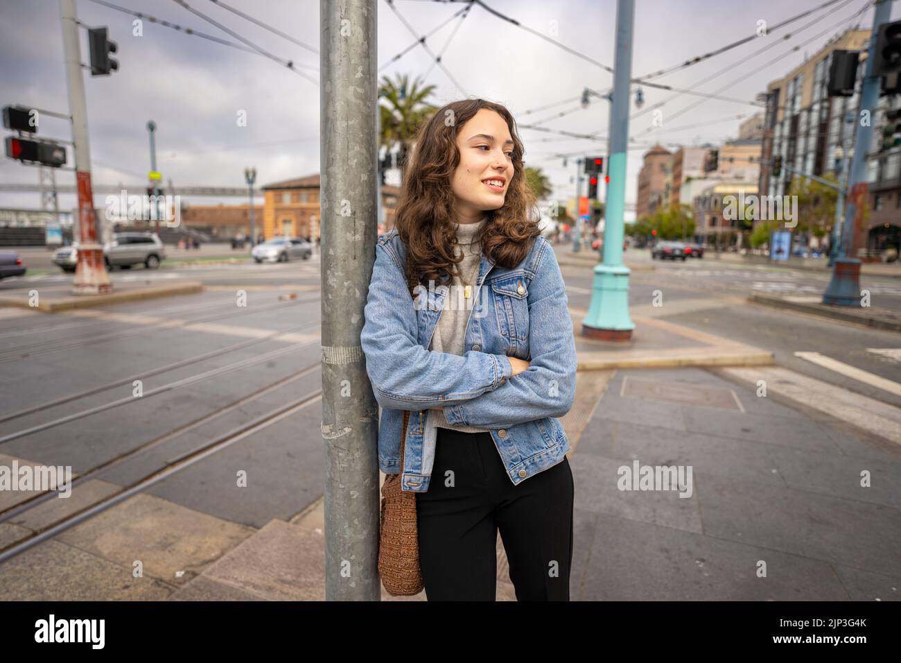 Ritratto senza posa di una bella giovane donna in attesa di attraversare una strada occupato Downtown | giacca in denim | San Francisco Wharf Foto Stock
