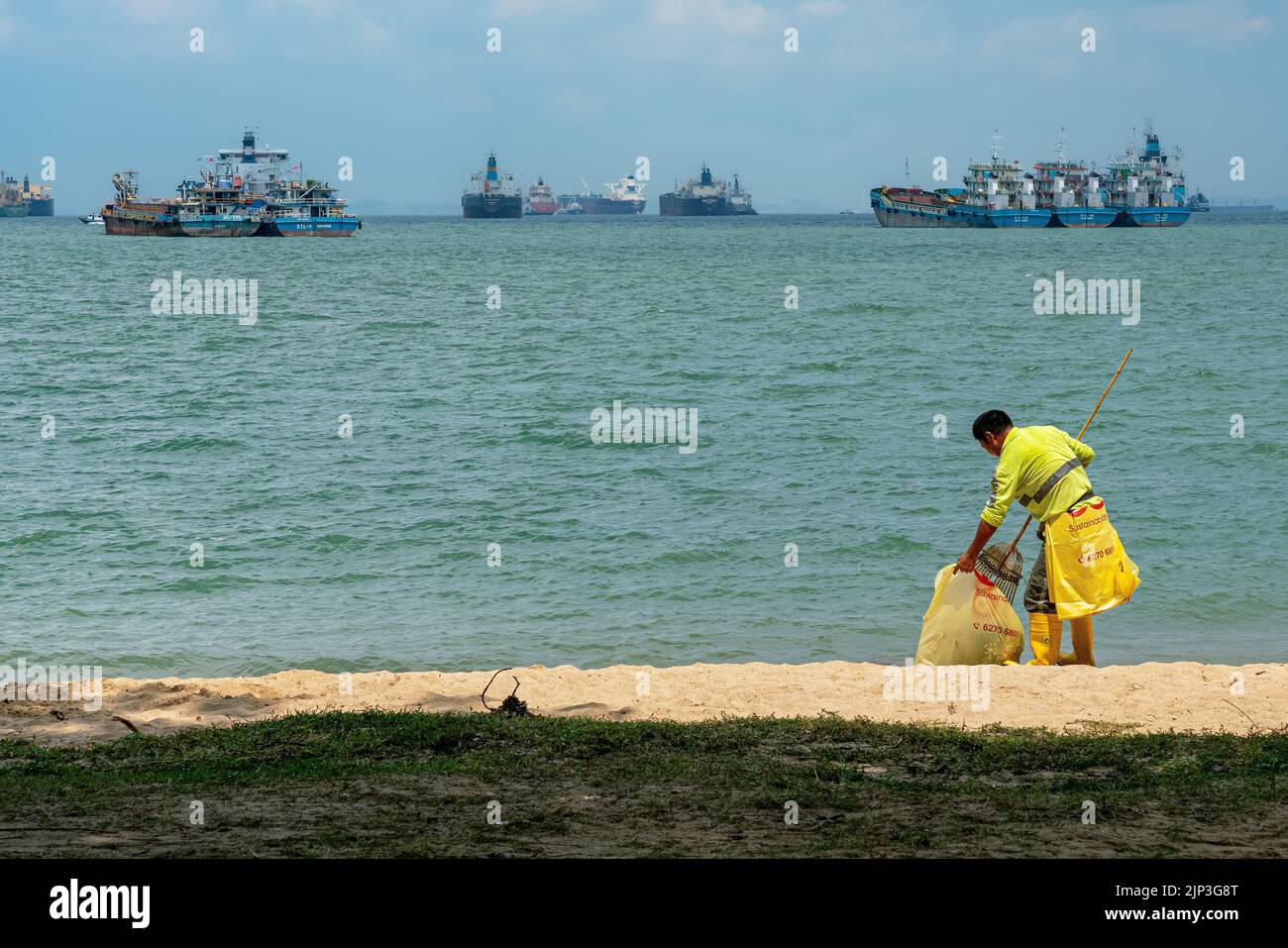 Un pulitore sta spazzando e schiarendo le foglie sulla spiaggia all'East Coast Park, Singapore. Copia spazio. Foto Stock