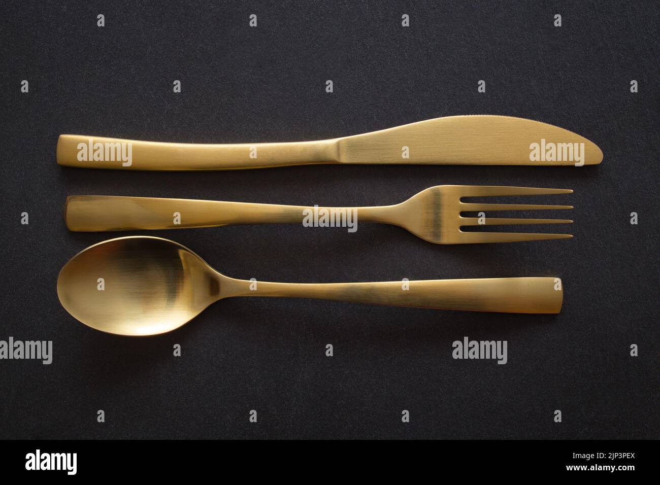Coltello, forchetta e cucchiaio d'oro su sfondo di pietra nera - fotografia del concetto alimentare Foto Stock