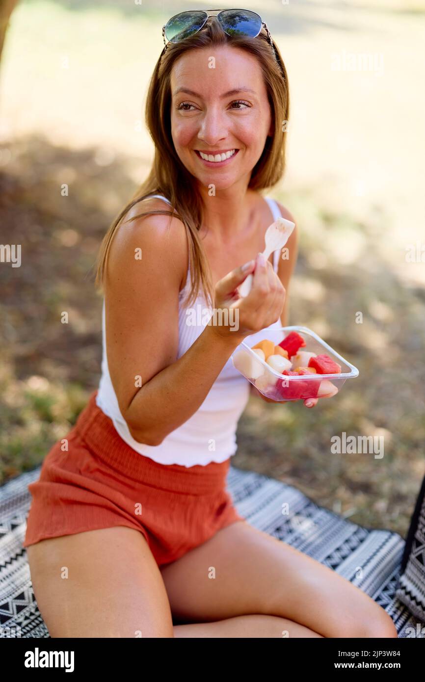 Donna seduta rilassante mangiare frutta fresca all'aperto Foto Stock