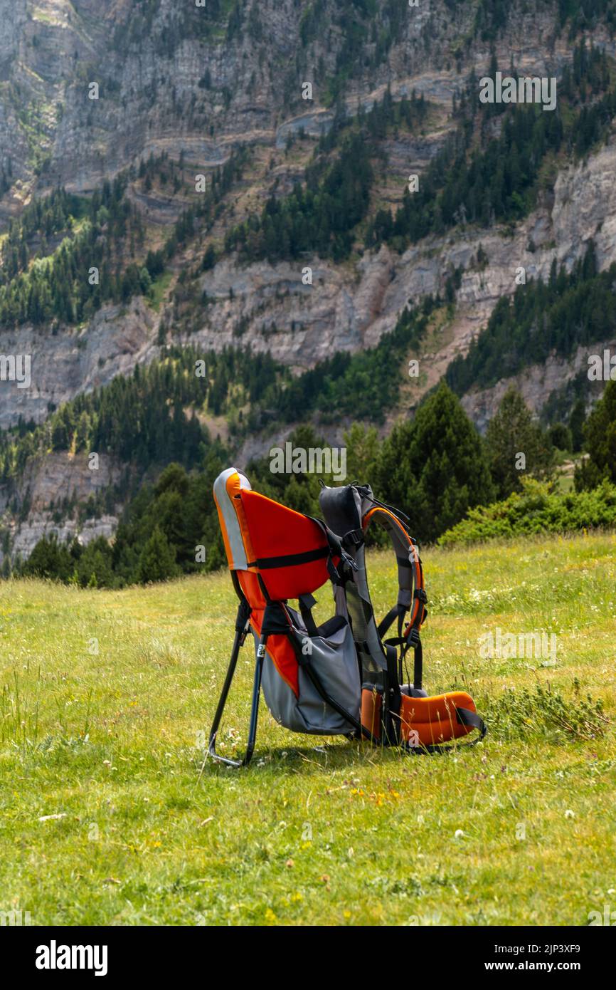 Uno zaino porta-bambino posizionato su un campo circondato da montagne, tiro verticale Foto Stock