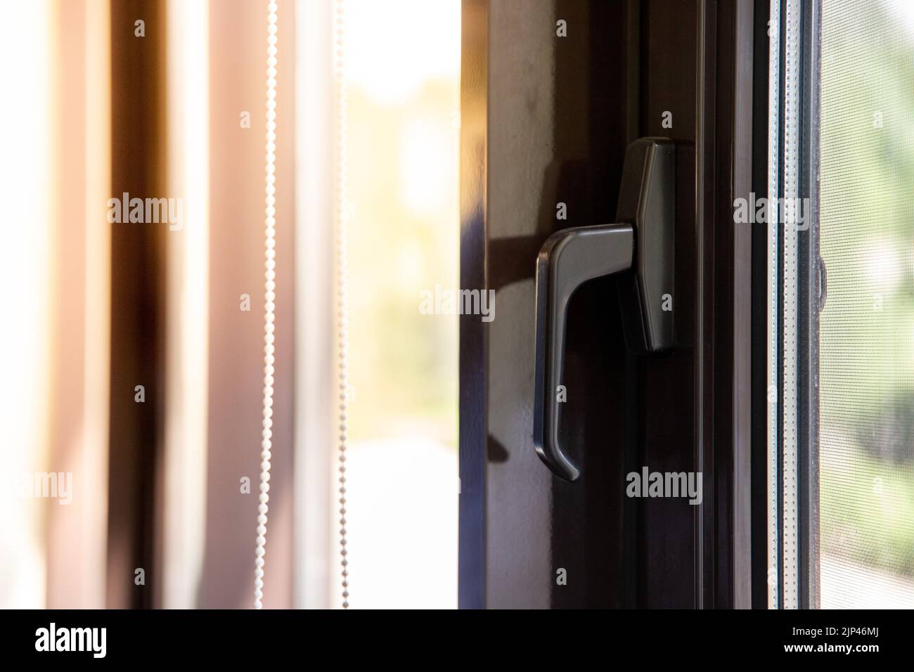 Maniglia per finestra su una finestra marrone in metallo-plastica attraverso la quale splende il sole Foto Stock