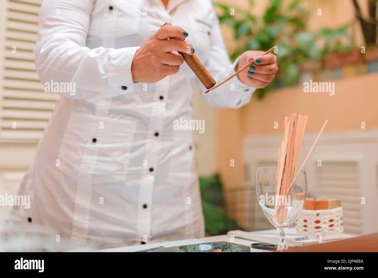 Una donna che illumina un sigaro con un pezzo di legno e vestita con una guayabera bianca Foto Stock