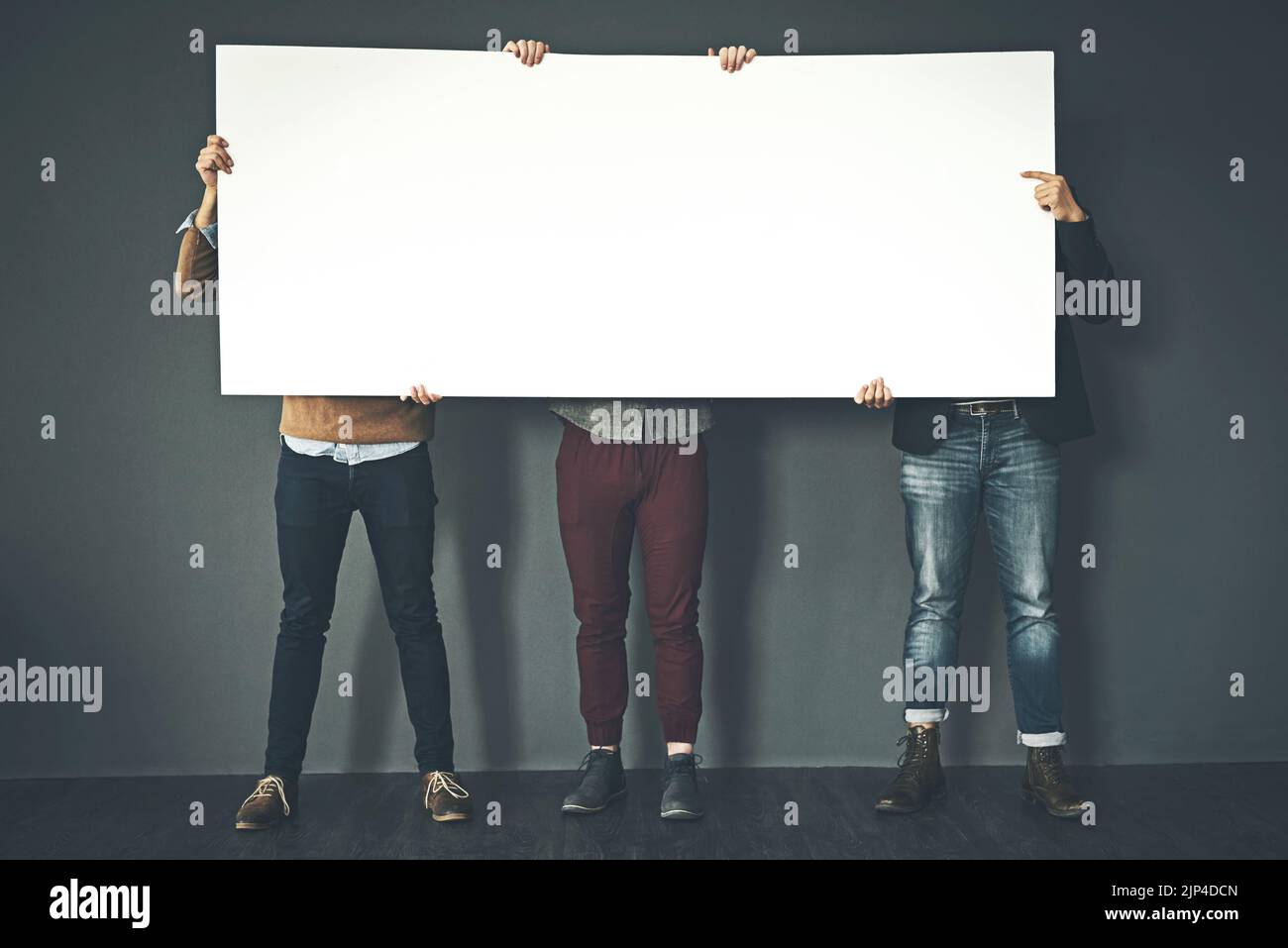 Gruppo di uomini d'affari che tiene in mano un segno copyspace che esprime la loro opinione sul lavoro con uno sfondo grigio. Persone con pubblicità in bianco poster Foto Stock