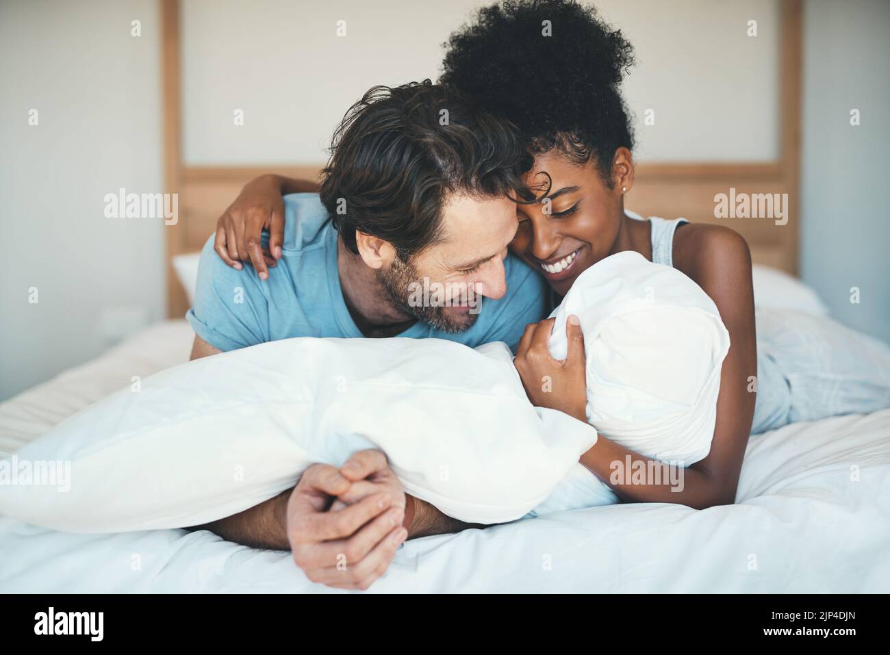 Divertente coppia interracial ridere, legarsi e sdraiarsi sul letto in una camera da letto casa e guardare felice, in amore e giocoso. Sorridendo uomo e donna abbracciando e. Foto Stock