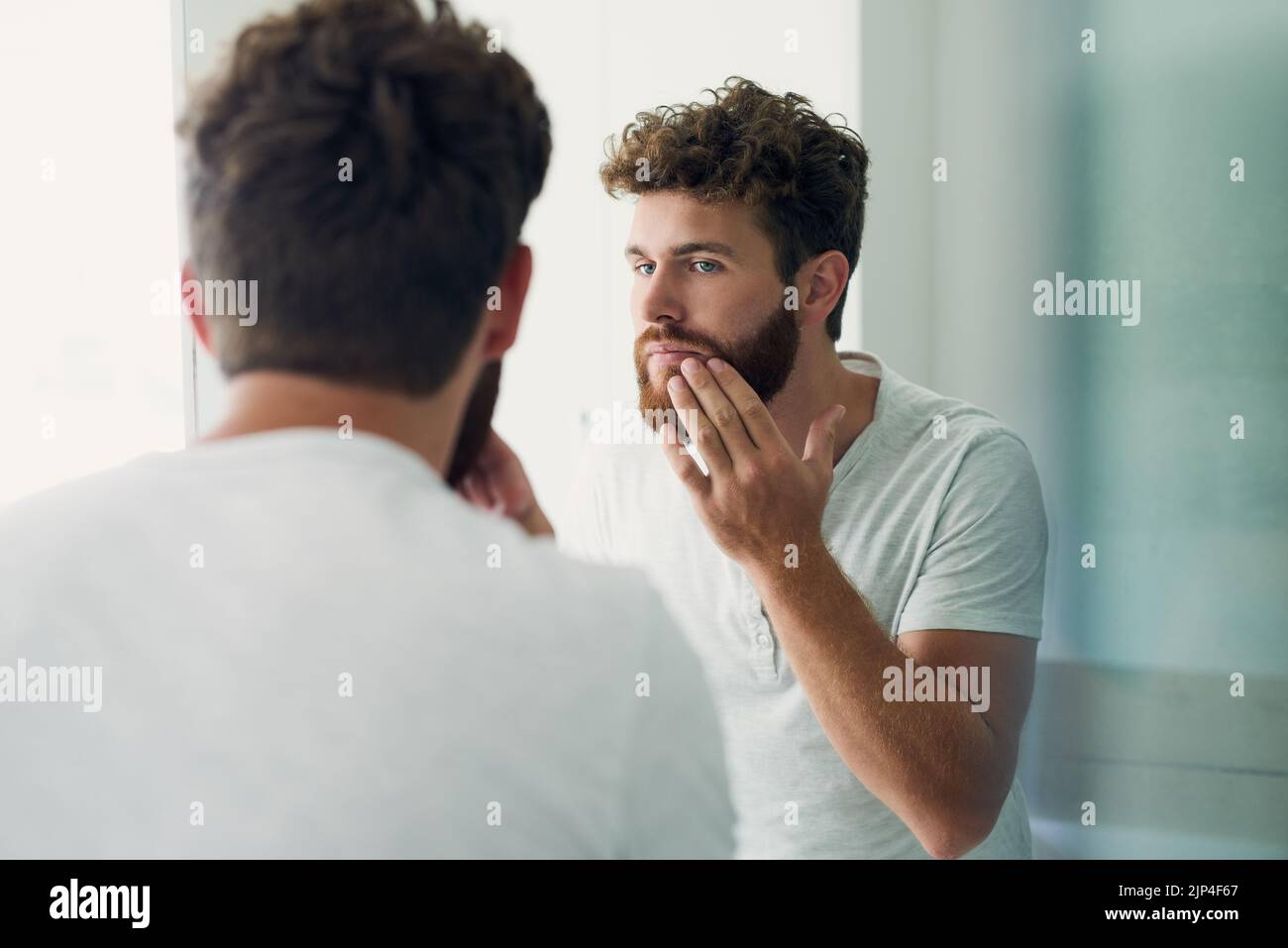 Controllare eventuali imperfezioni. Un bel giovane che controlla la pelle nello specchio del bagno. Foto Stock