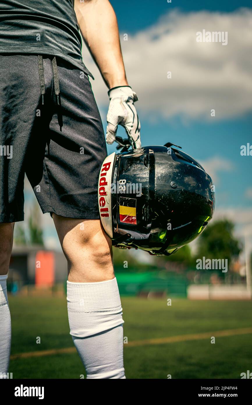 Un colpo verticale di un uomo che tiene con guanti bianchi nike, un casco da calcio americano belga Redbull contro le ginocchia Foto Stock