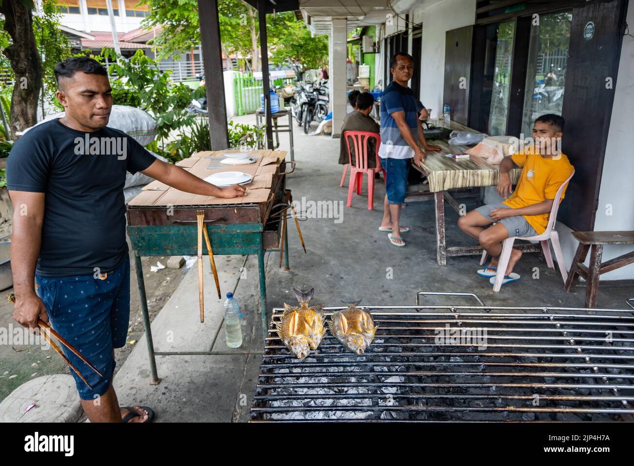 Un uomo locale griglia pesce su una griglia a carbone in un ristorante. Sulawesi, Indonesia. Foto Stock