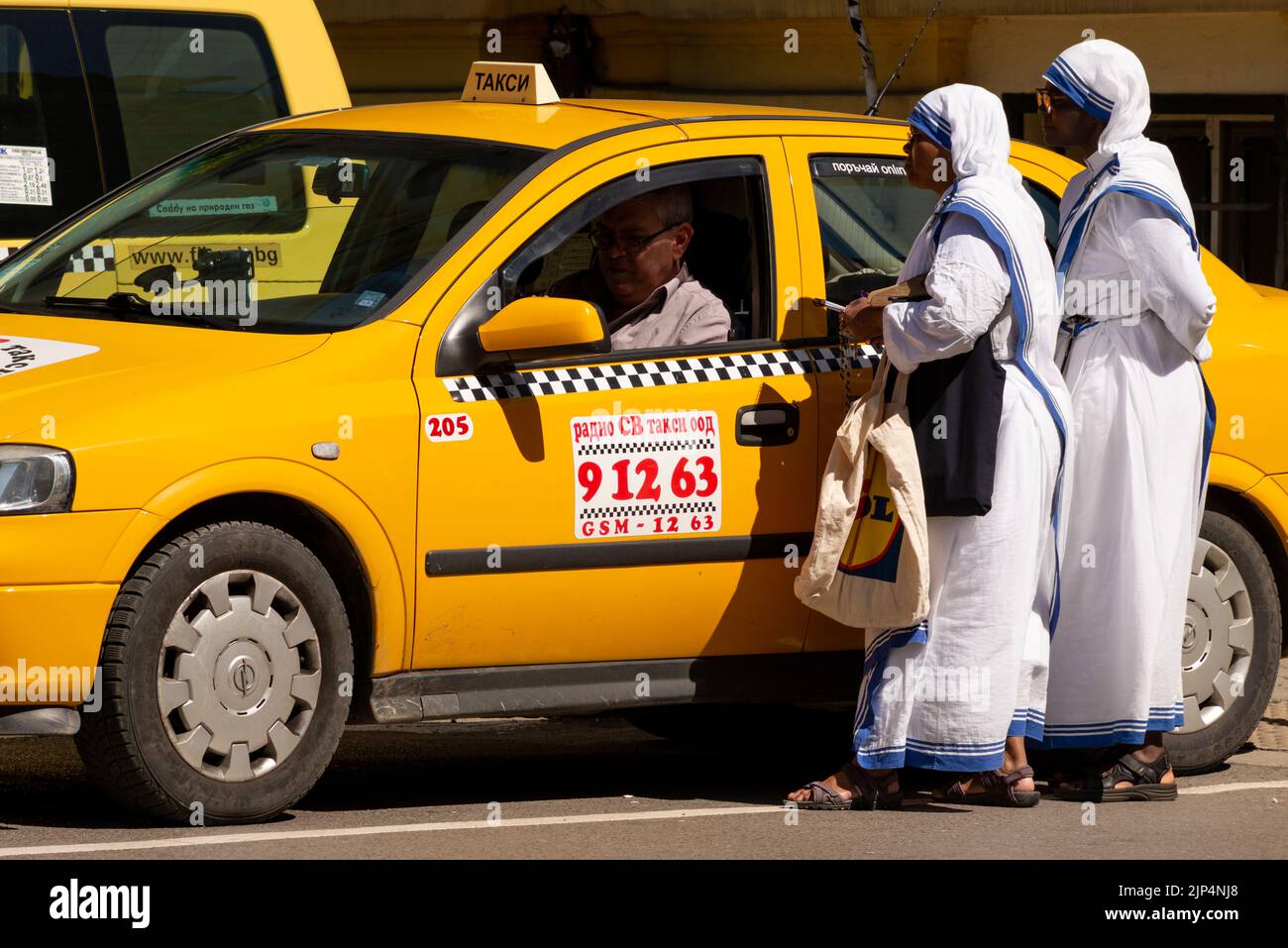 Suore africane in abiti bianchi che chiedono di fare un taxi giallo a Sofia, Bulgaria, Europa orientale, Balcani, UE Foto Stock