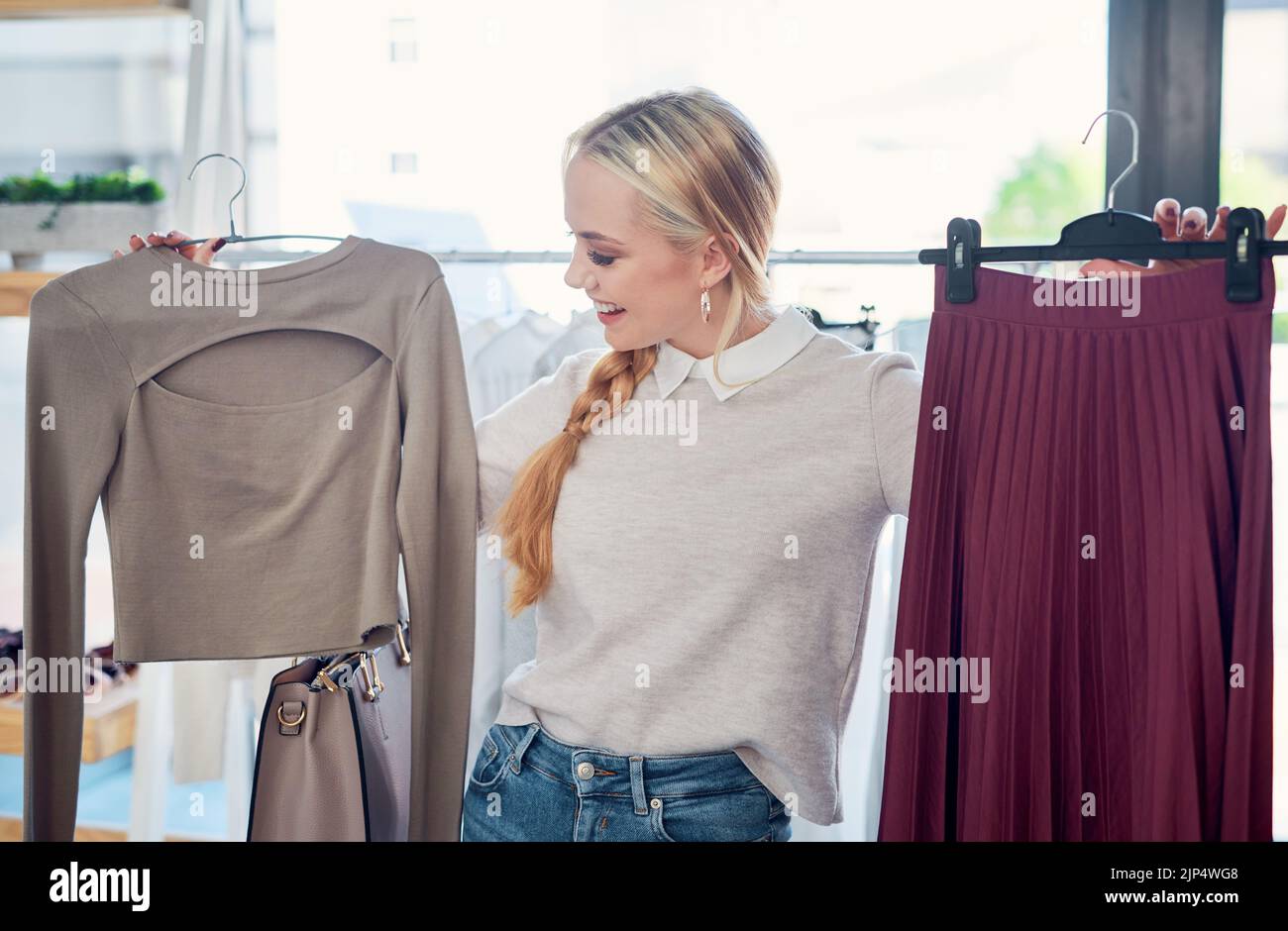 Bella giovane donna sorridente shopping in un moderno negozio di moda, guardando alla moda elegante stili di abbigliamento. Cliente caucasica felice Foto Stock