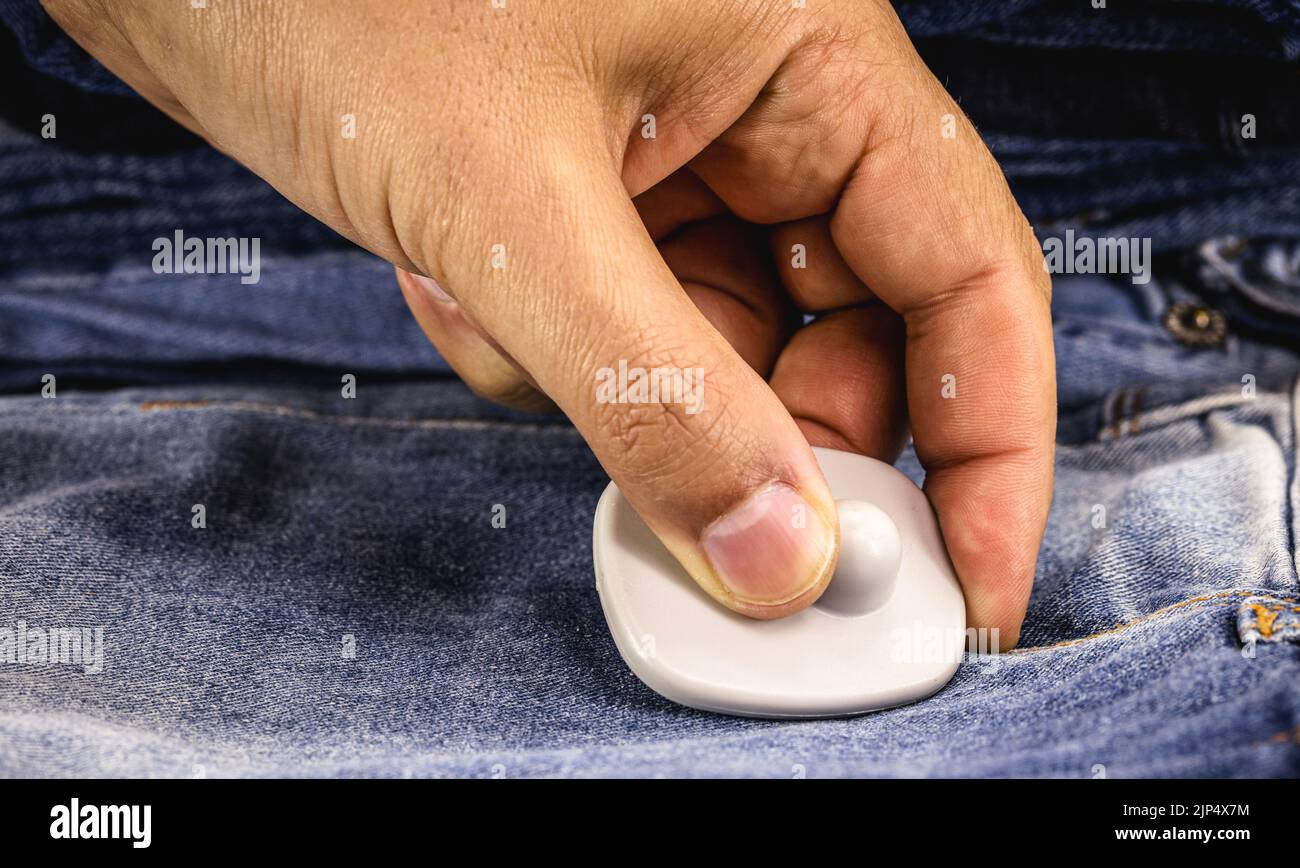 dispositivo anti-furto per la rimozione delle mani utilizzato in commercio, tag o tag anti-furto su abbigliamento denim, tentato furto in commercio Foto Stock