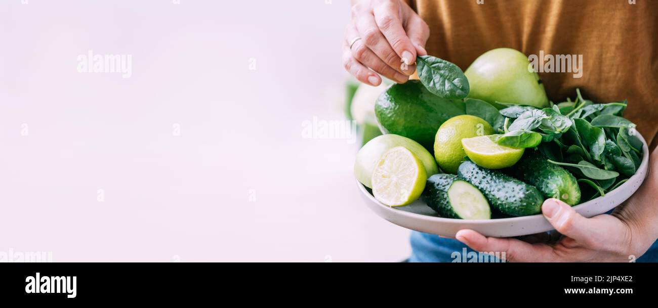 Una donna tiene nelle sue mani frutta fresca di verdure verdi in grande piatto, spazio di copia di sfondo chiaro Foto Stock