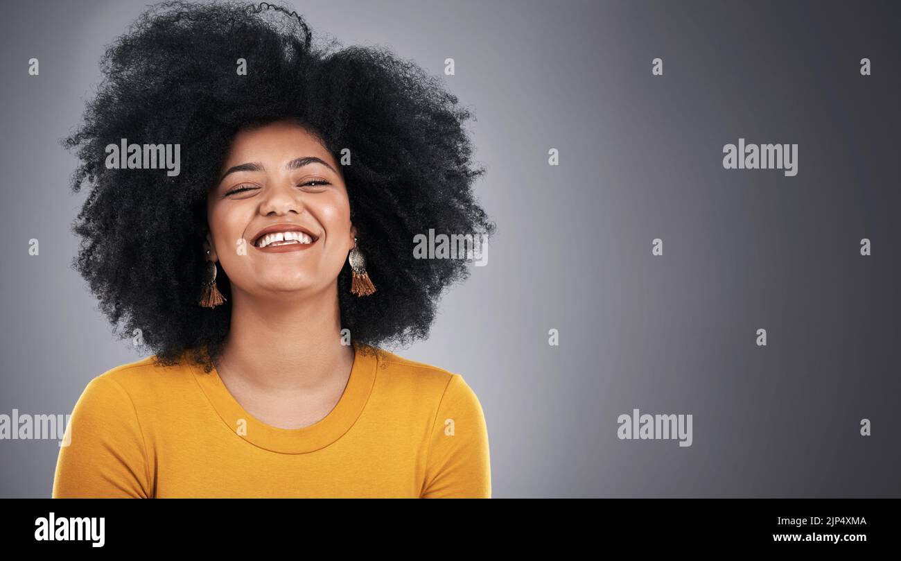 I suoi capelli grandi aggiungono un po' di luce. Studio di una giovane donna attraente che posa su uno sfondo grigio. Foto Stock