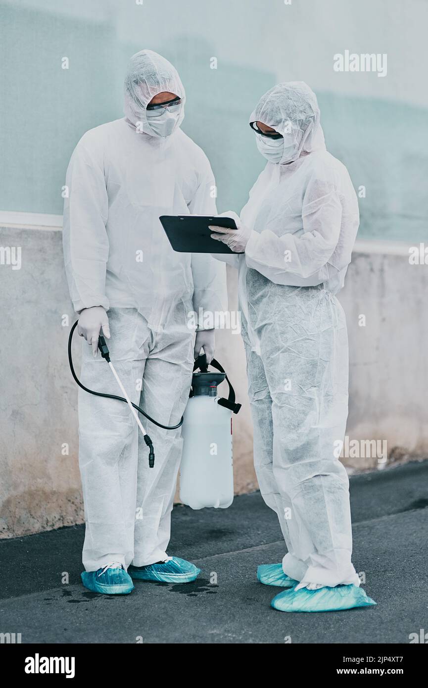 Operatori sanitari che puliscono fuori di un edificio utilizzando un elenco per seguire le istruzioni sulla sicurezza a rischio biologico durante il covid. Ricercatori medici indossando Foto Stock